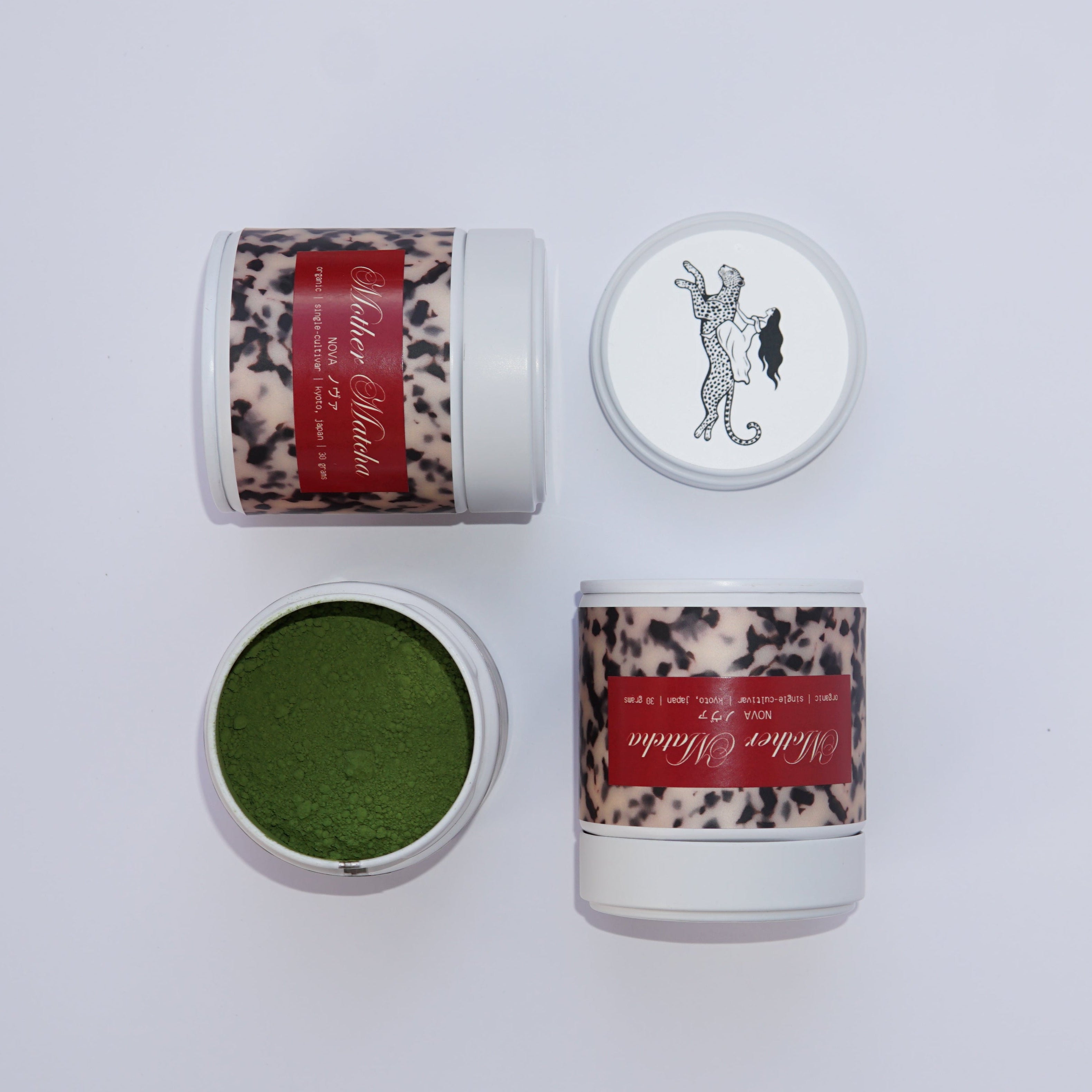 Three matcha tins arranged on a light gray background: one open tin showing bright green matcha powder, two closed tins with a leopard-print label and red band, and one open lid with a black line drawing of a woman riding a leopard.